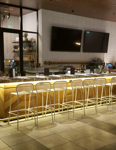 A bar in a restaurant with stools and a tv.