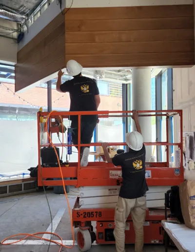 Two men on a lift working on the ceiling of a building.