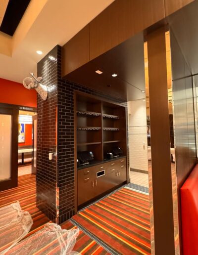 A built-in shelf unit with several black toasters is set against a black tiled wall in a brightly lit room with red and orange striped carpet.