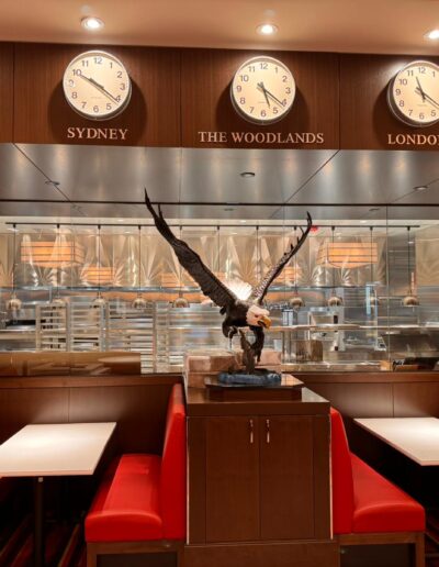 A restaurant booth with red seating, a large eagle statue in the center, five clocks above showing different cities, and a visible kitchen in the background.